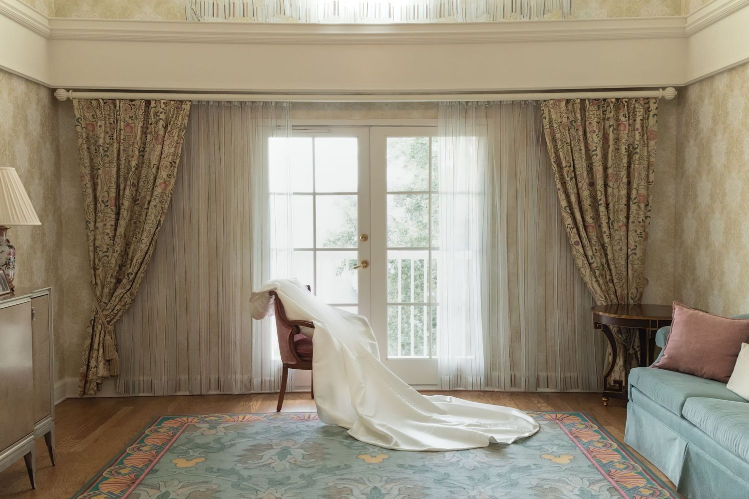 An elegant bridal suite with flowing curtains and a wedding dress train displayed on hardwood floors.