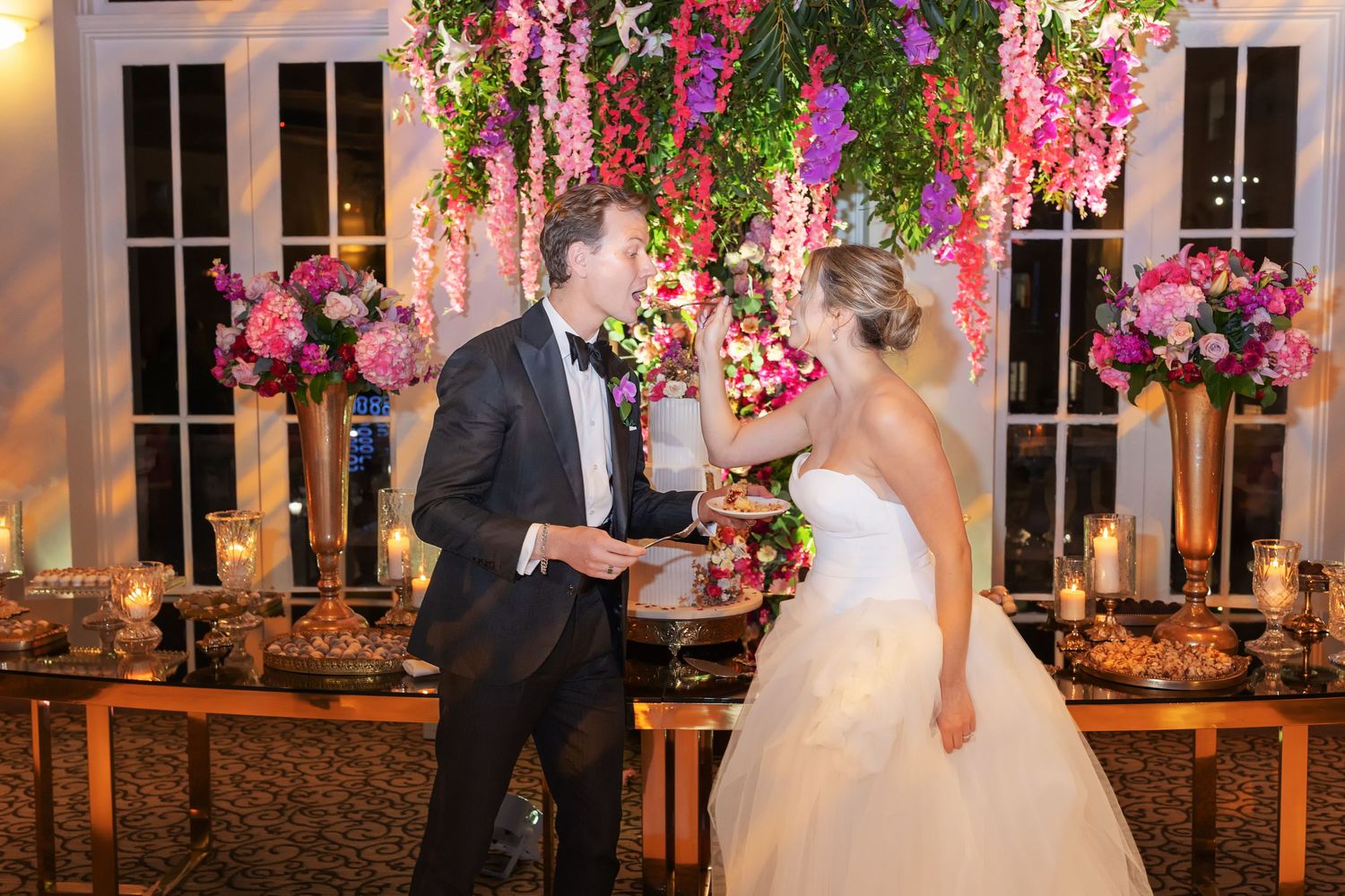 Bride and groom share a romantic moment under lush floral arrangements at an elegant wedding reception.
