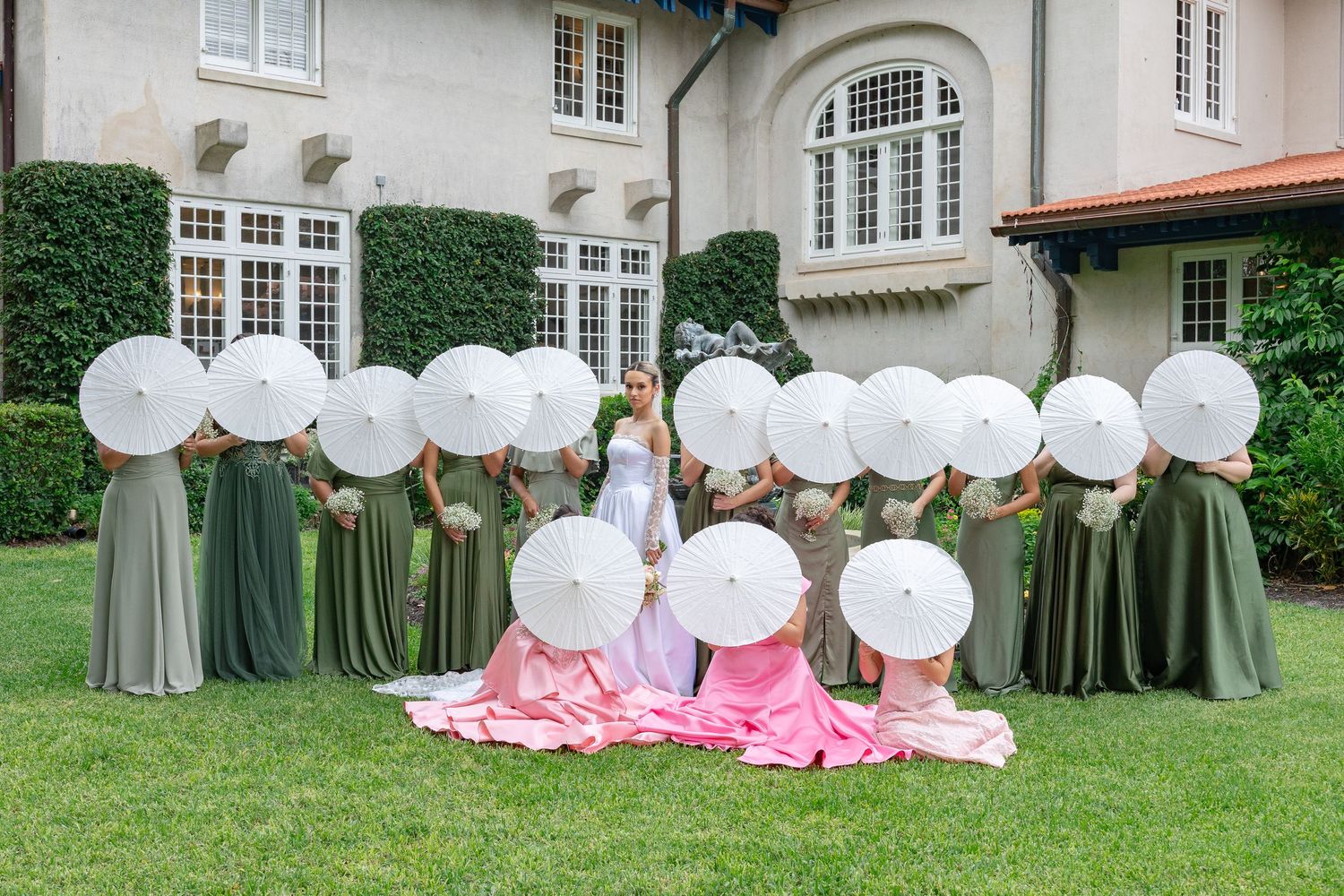 Wedding party members hold white balloons in front of their faces while posing for a creative outdoor group photo.