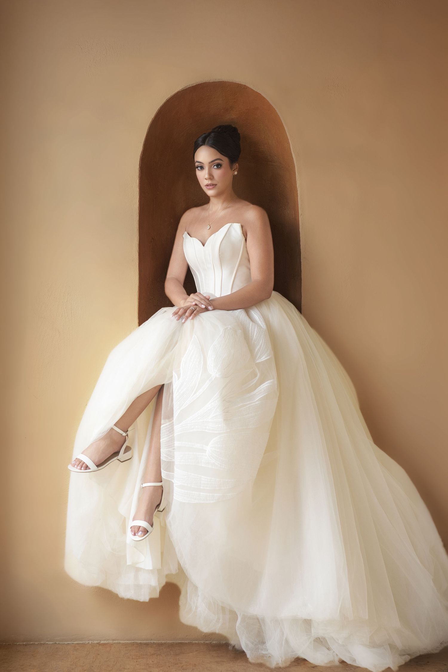 Elegant bride in a strapless white ballgown with corset bodice and tulle skirt, posing in an arched alcove.