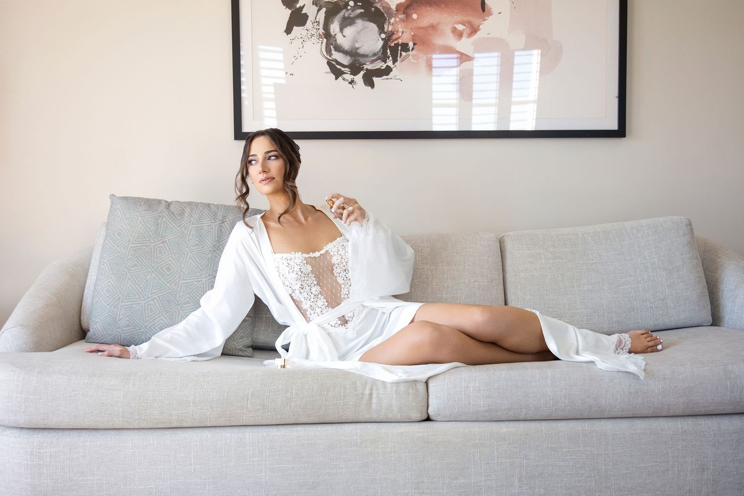 Woman in white loungewear relaxes on a light gray couch in a modern living room setting.