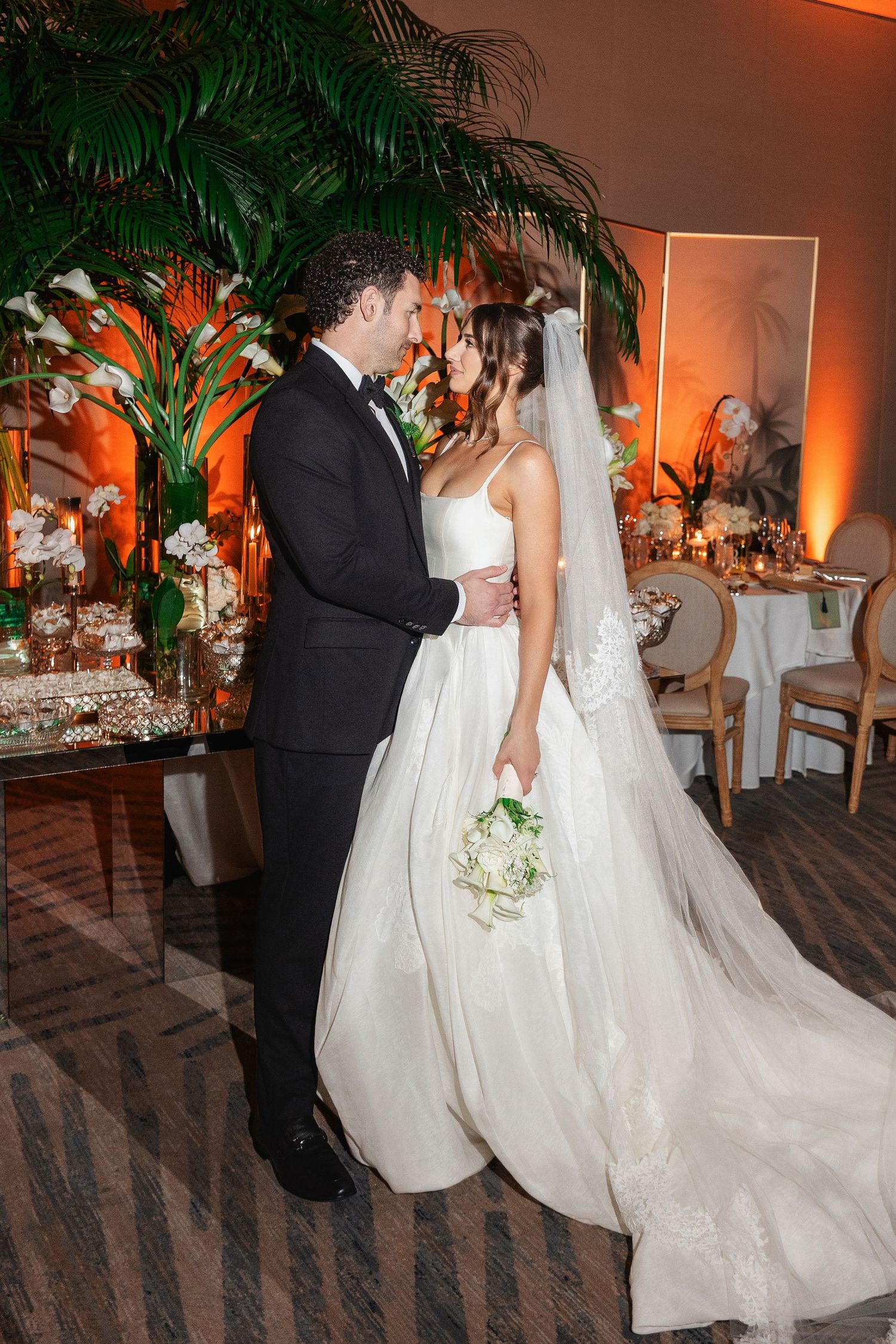 Bride in white ball gown with veil and groom in tuxedo share first dance at elegant wedding reception.