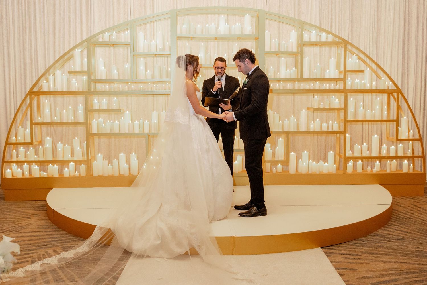 Bride and groom exchange vows at elegant wedding altar with gold arch backdrop and officiant.