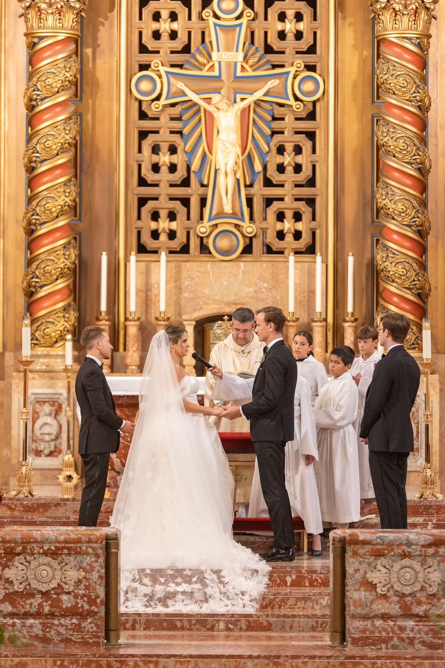 Bride and groom exchanging vows at ornate church altar with golden crucifix and candles during wedding ceremony.