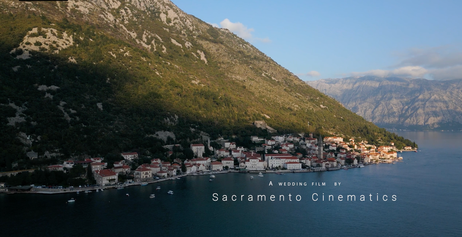 Coastal village nestled along mountainous shoreline with calm waters and dramatic landscape at sunset.
