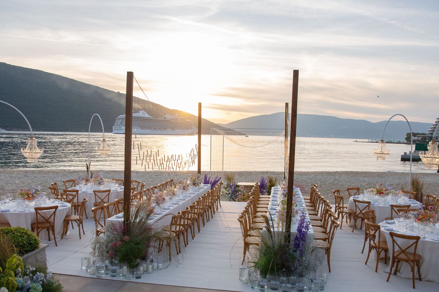 Elegant beach wedding setup with wooden chairs and mountain views at sunset.