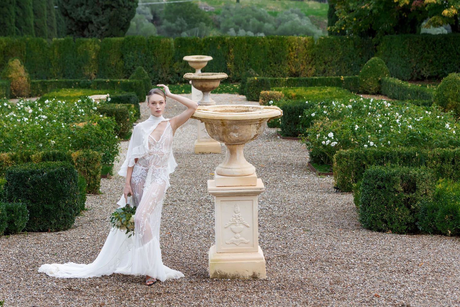 Wedding dress photographed in sequence along a formal garden path with stone features.
