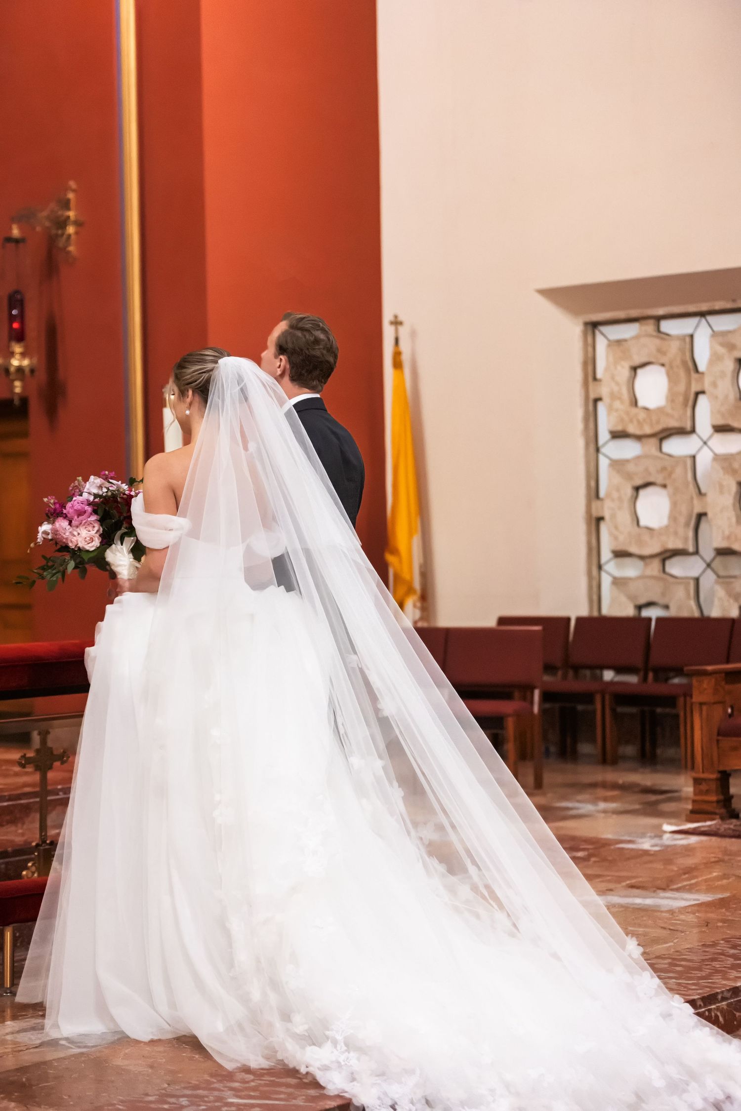 Bride and groom standing at church altar during wedding ceremony, bride wearing long white gown with flowing veil.