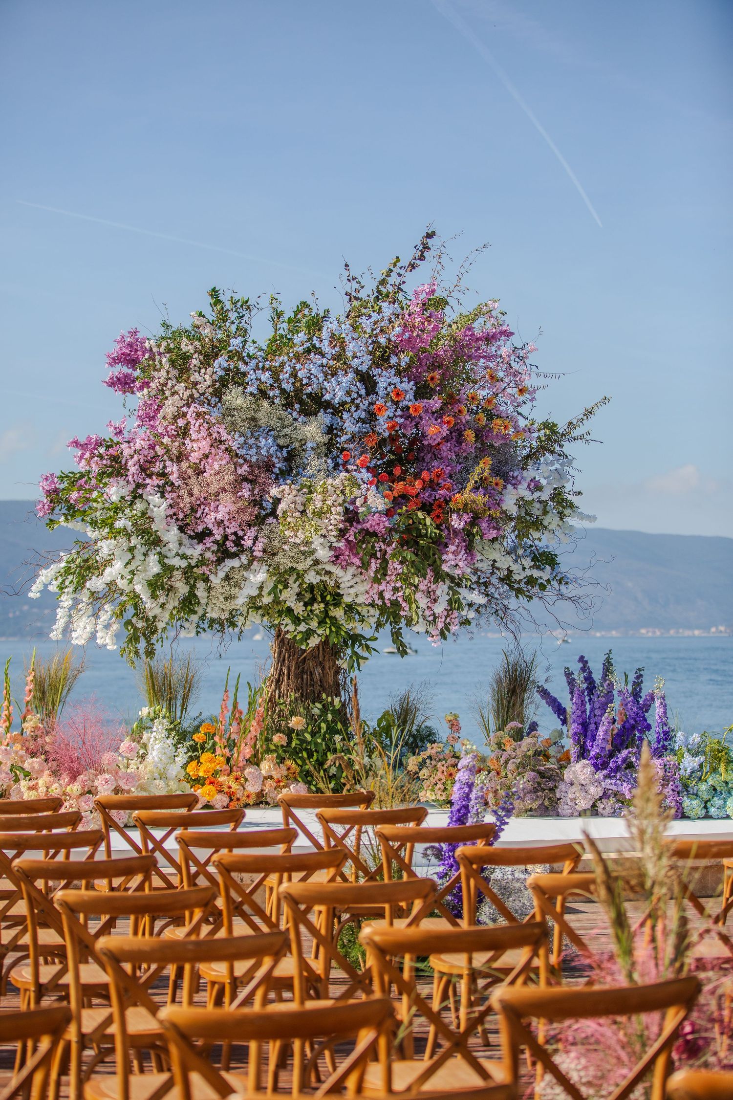 Outdoor wedding ceremony setup with wooden chairs and vibrant floral arrangements overlooking a waterfront view.