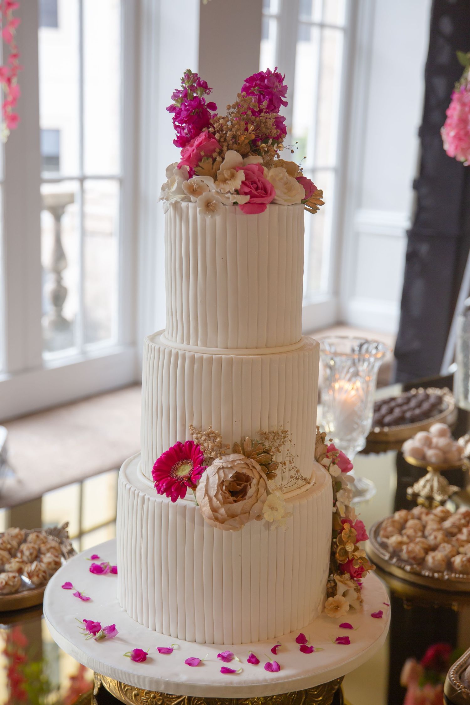 Elegant three-tier white wedding cake with pink and blush floral decorations on a gold stand.