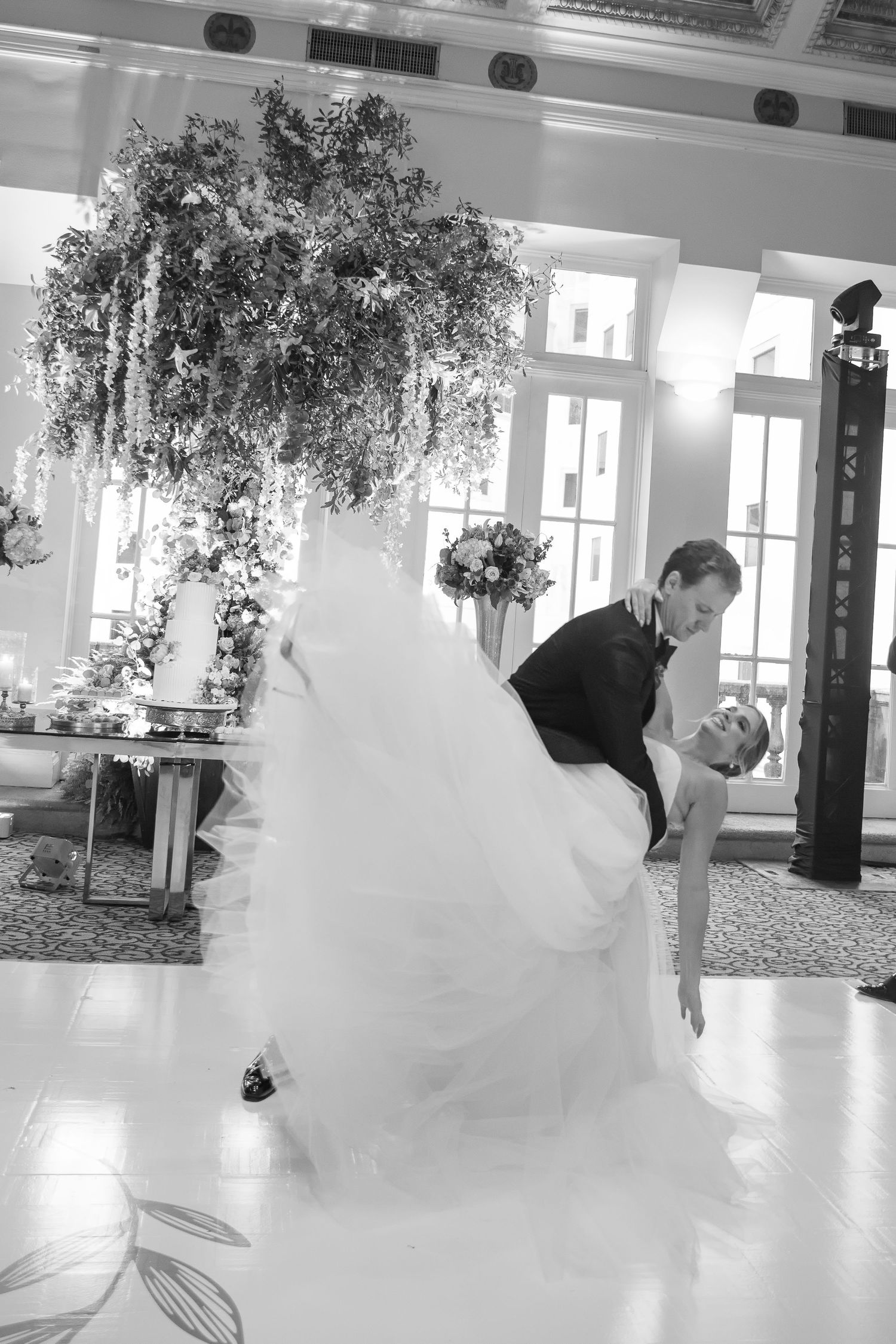 Black and white photo of a groom dipping his bride during their first dance at an elegant wedding reception.