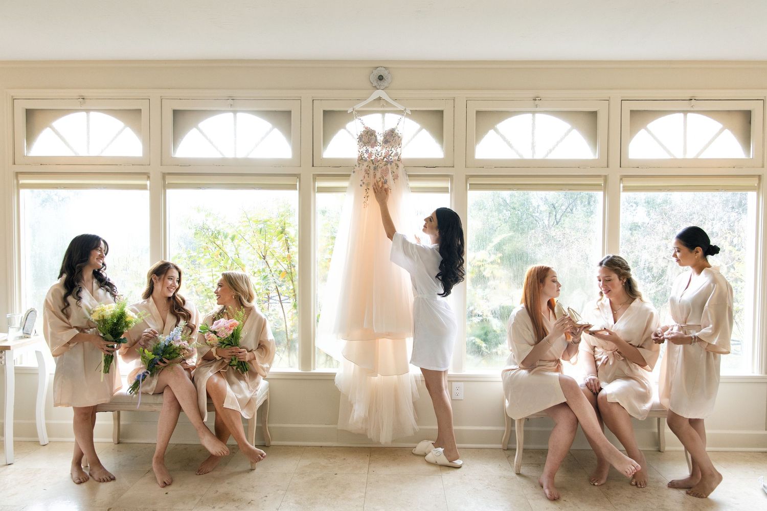 Fun bridal party photo series showing playful poses along white windows in a bright room.