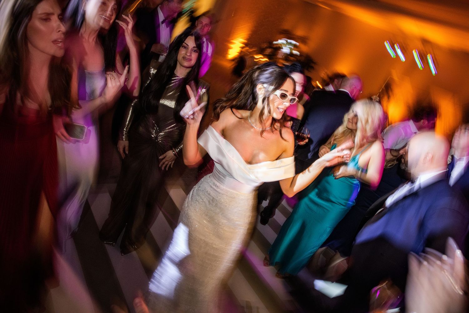 People dancing and celebrating at a lively party with warm orange lighting and motion blur effects.