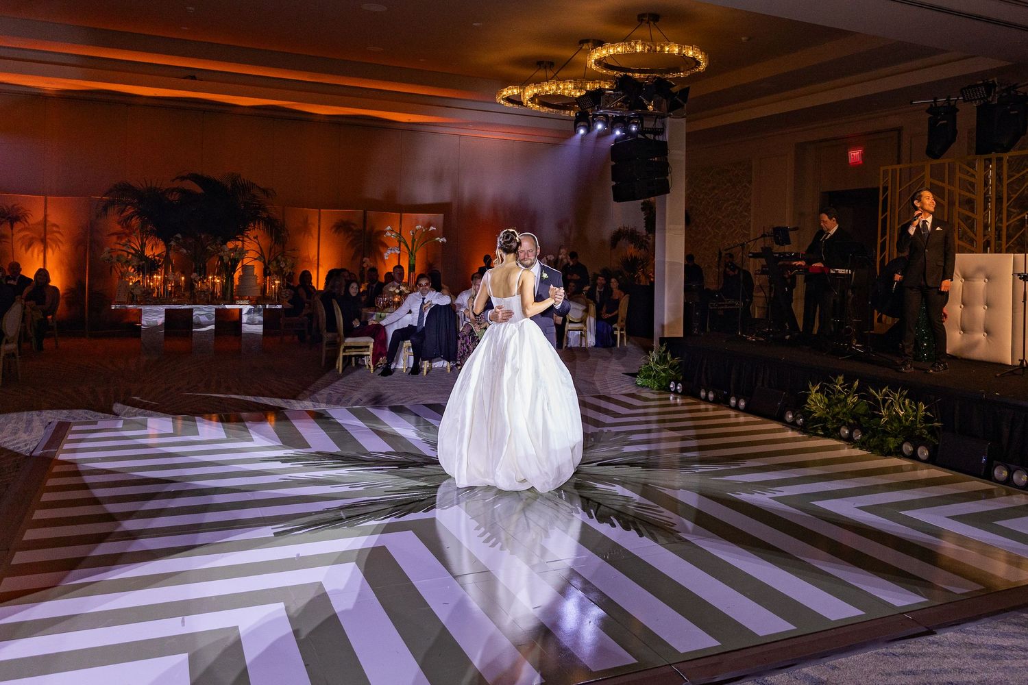 Bride and groom share first dance on striped black and white dance floor at elegant wedding reception.