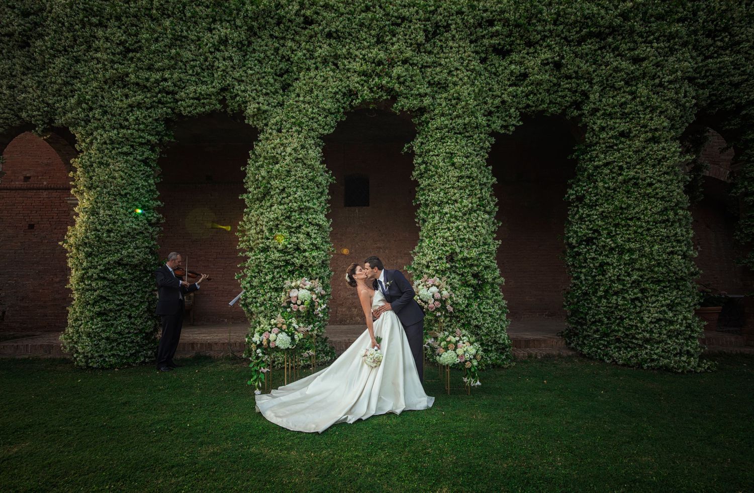 Wedding dress photographed against lush green ivy-covered walls in a garden setting.