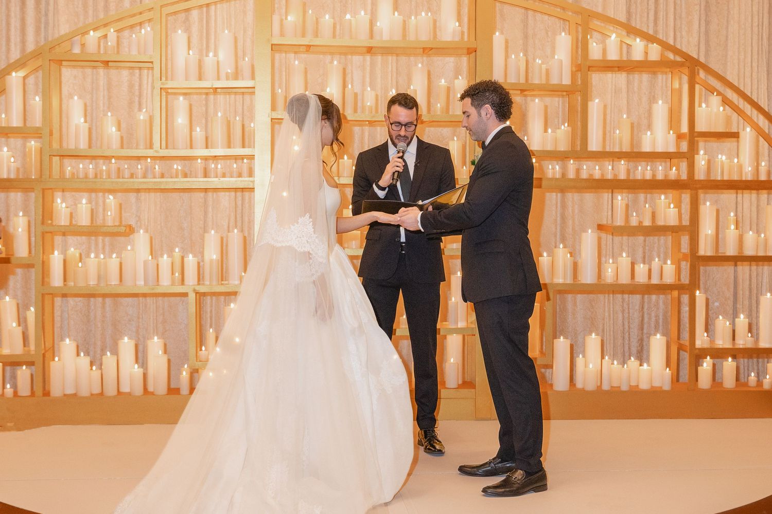 Bride and groom exchanging vows at elegant candlelit wedding ceremony altar with officiant.