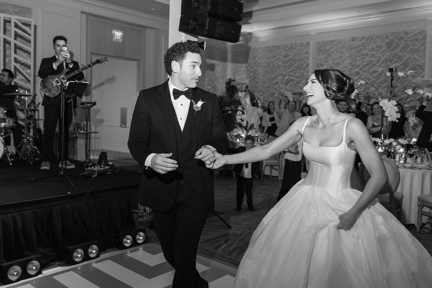 Black and white photo of bride and groom sharing first dance at elegant wedding reception with live band performing.
