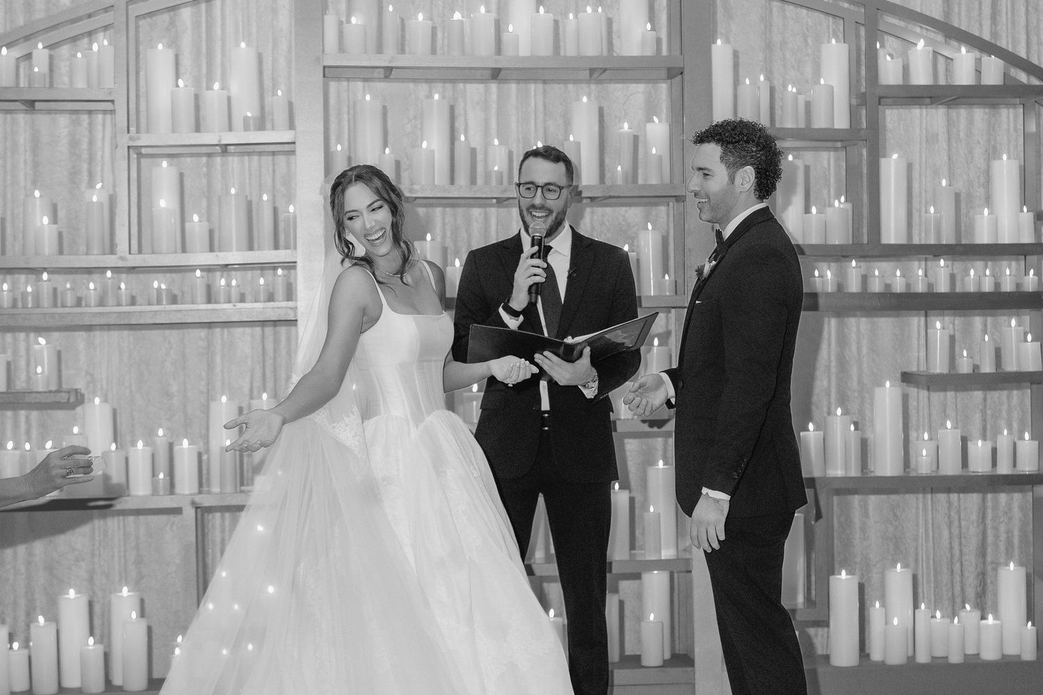 Black and white wedding ceremony photo with bride, groom, and officiant surrounded by glowing candles.