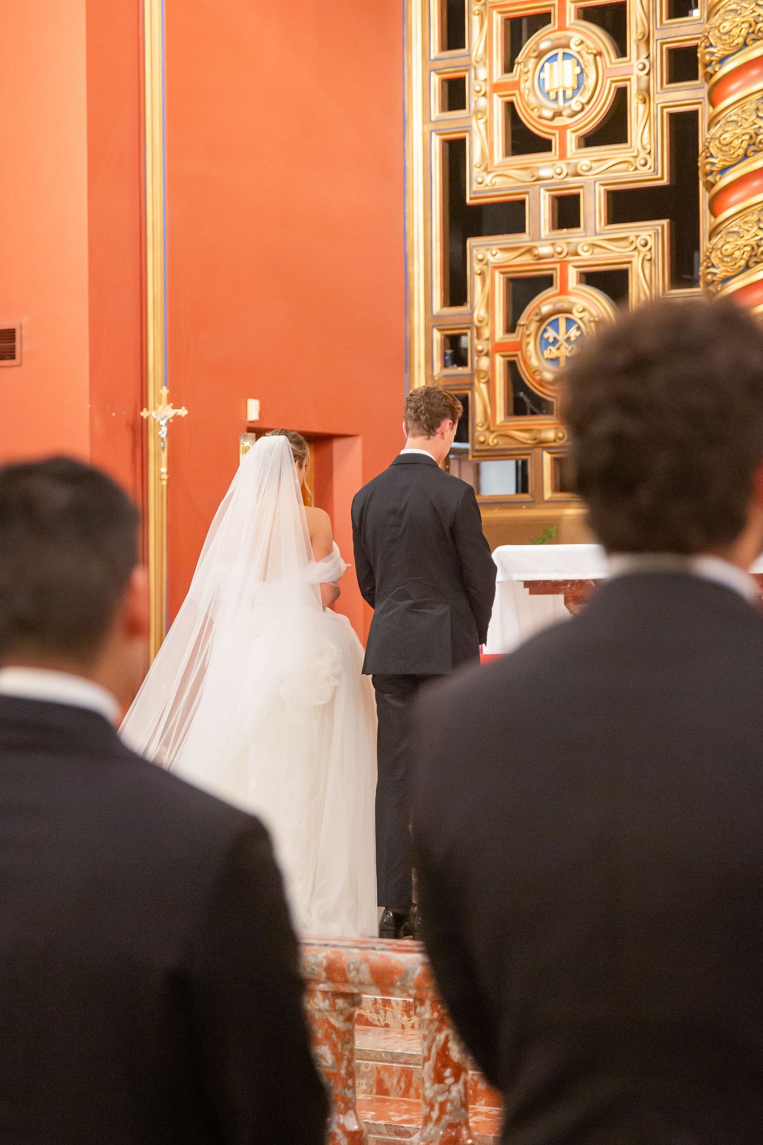 Bride and groom stand at church altar during wedding ceremony, guests watching from behind.