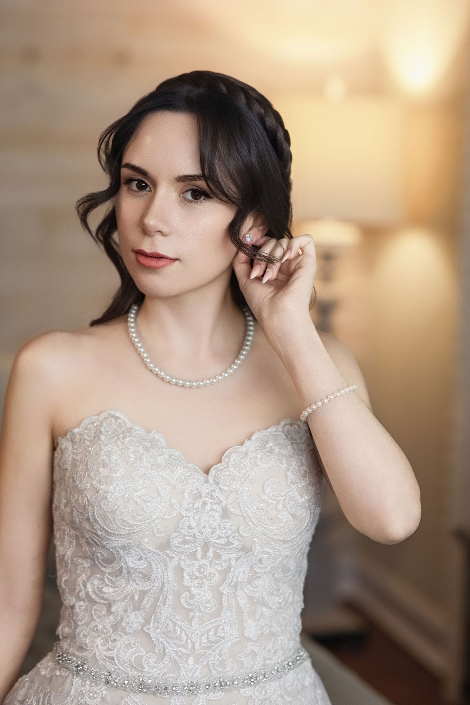 Close-up details of an ornate white lace wedding dress with pearl necklace accessories.