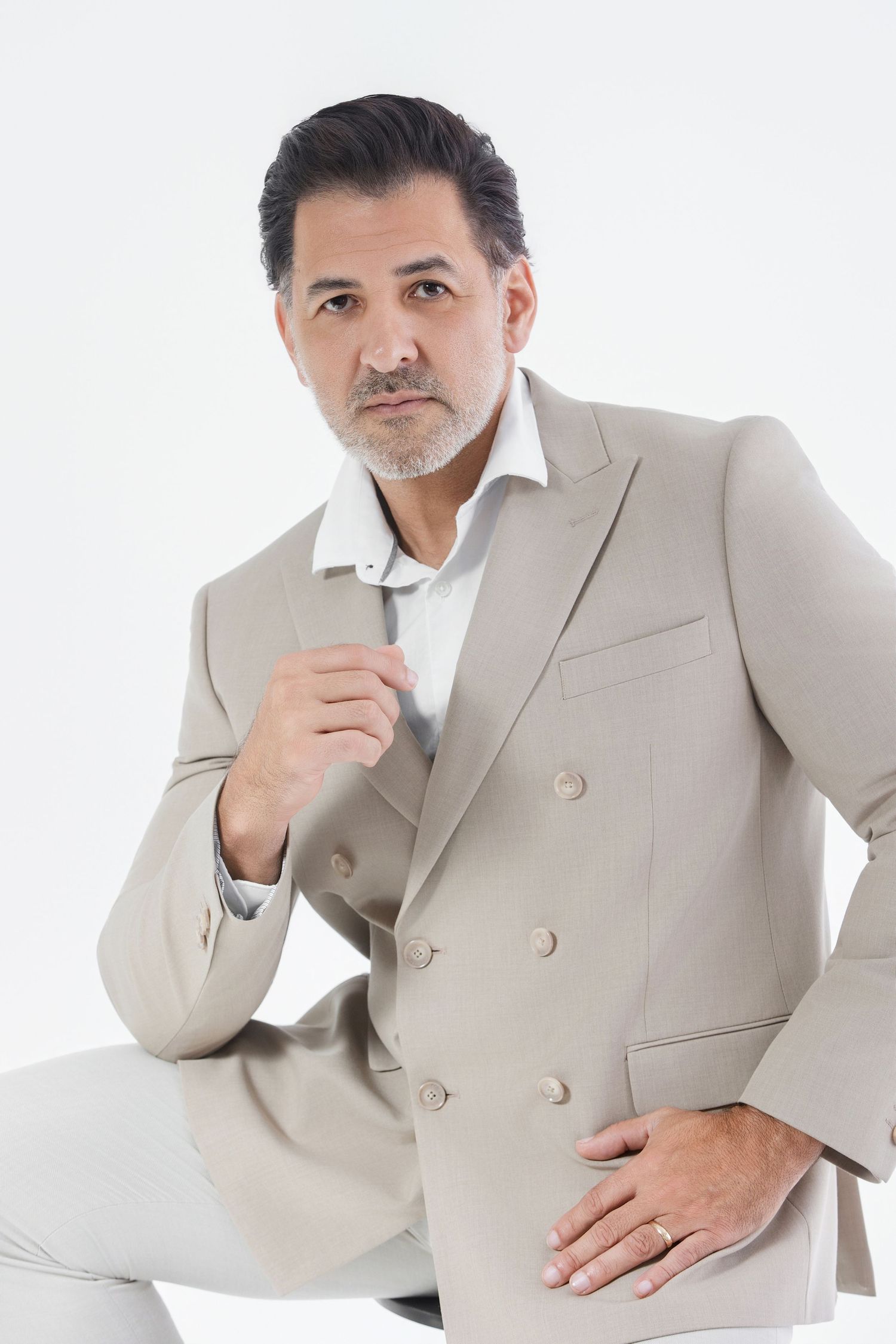 Middle-aged man in beige double-breasted suit poses confidently against white background.