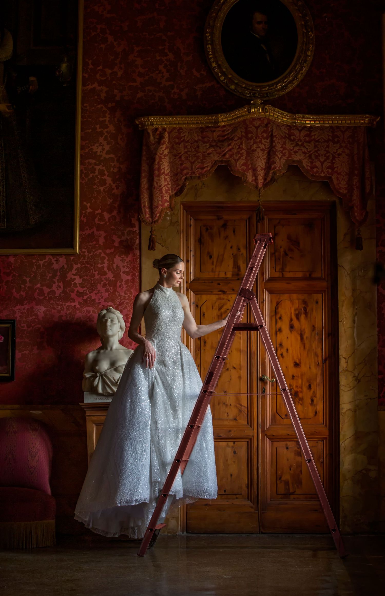 Figure in vintage lace gown poses in ornate room with red wallpaper and antique wooden doors.