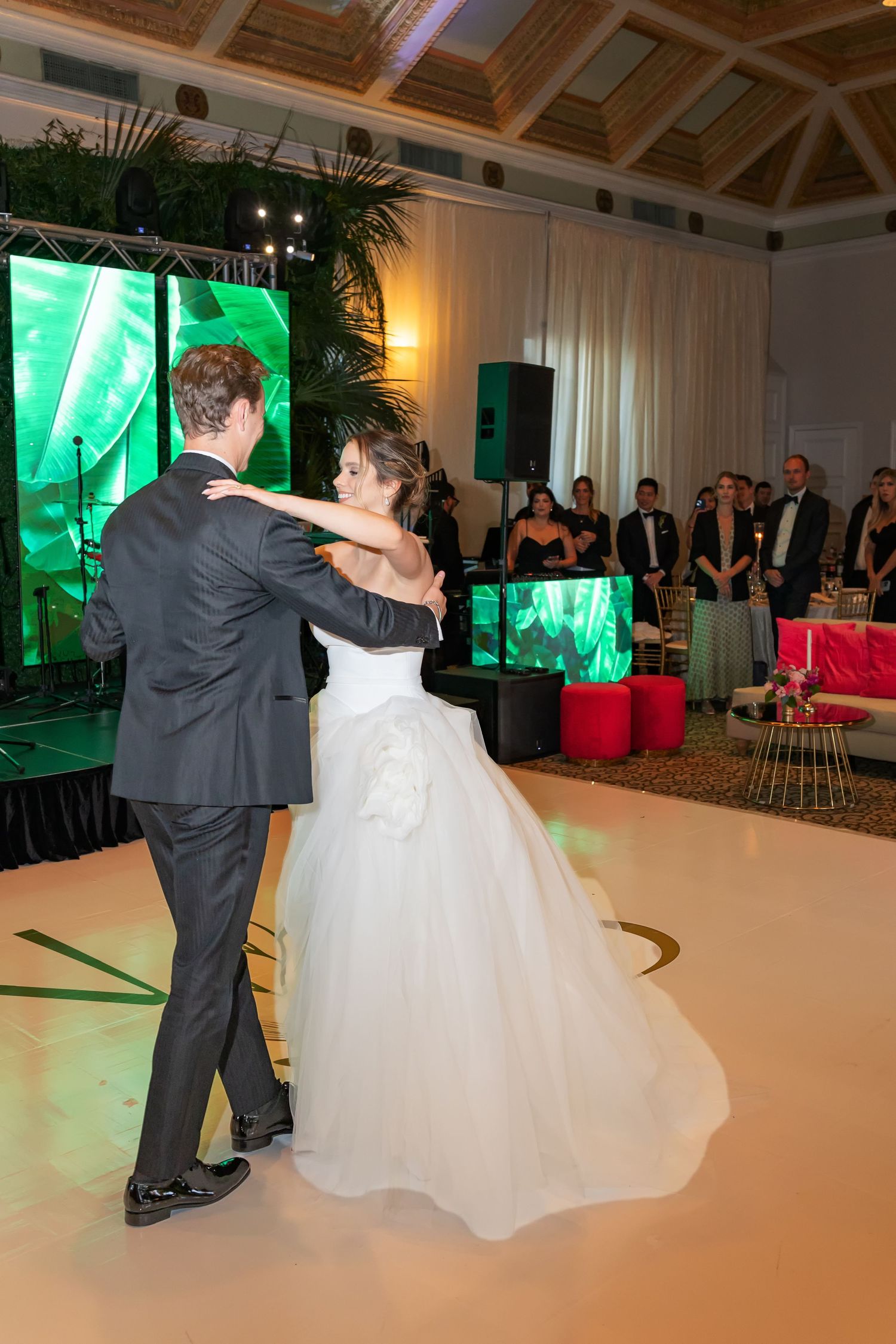 Bride and groom share their first dance on a white dance floor at an elegant wedding reception.