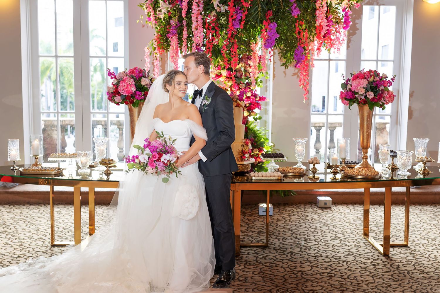 Bride and groom share a romantic kiss beneath a stunning floral ceiling installation of pink and fuchsia blooms at their wedding reception.