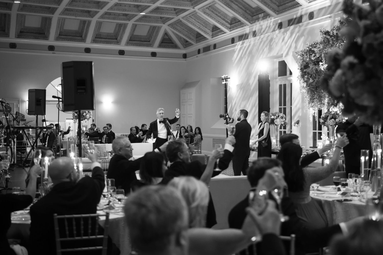 Elegant black and white wedding reception with guests dining while speaker addresses the crowd.