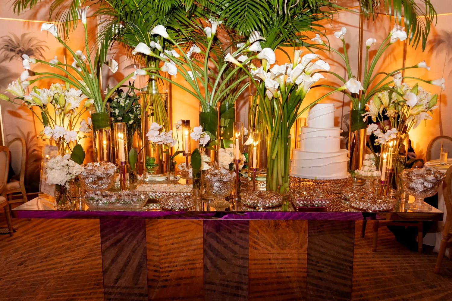 Elegant wedding reception table with tall white calla lily centerpieces, candles, and crystal glassware on a purple linen.