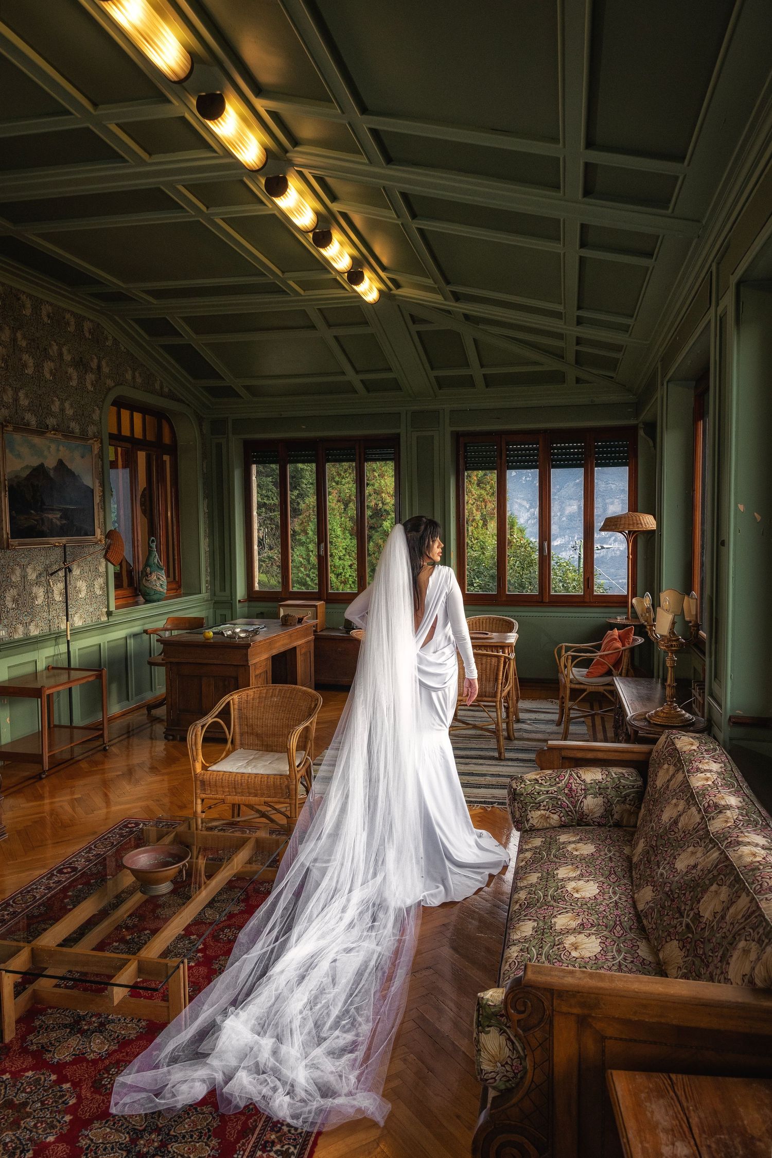 Wedding dress flowing dramatically in vintage green-walled room with period furniture.