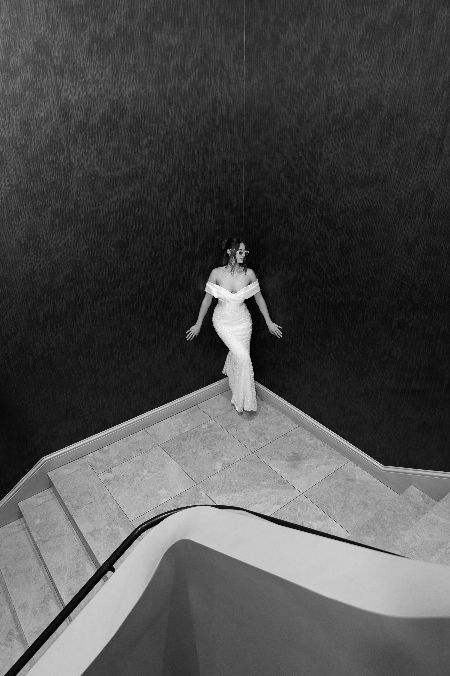 A black and white photo sequence shows a figure in white dress descending angular geometric stairs.