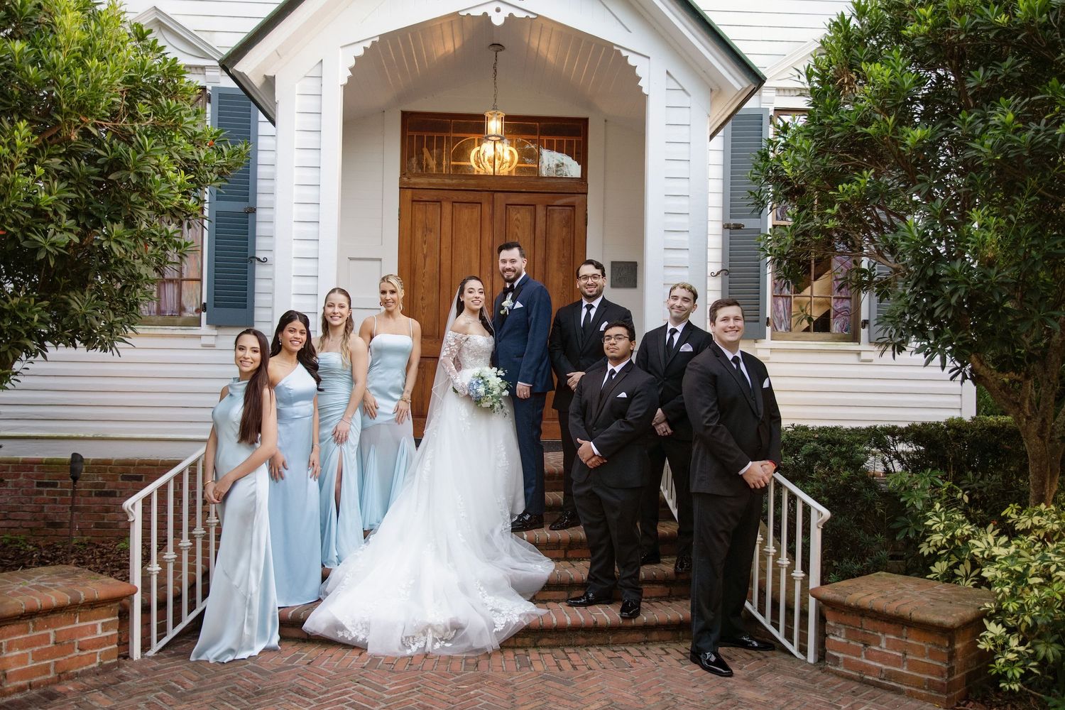 Wedding party poses on the steps of a classic white house with traditional architecture.