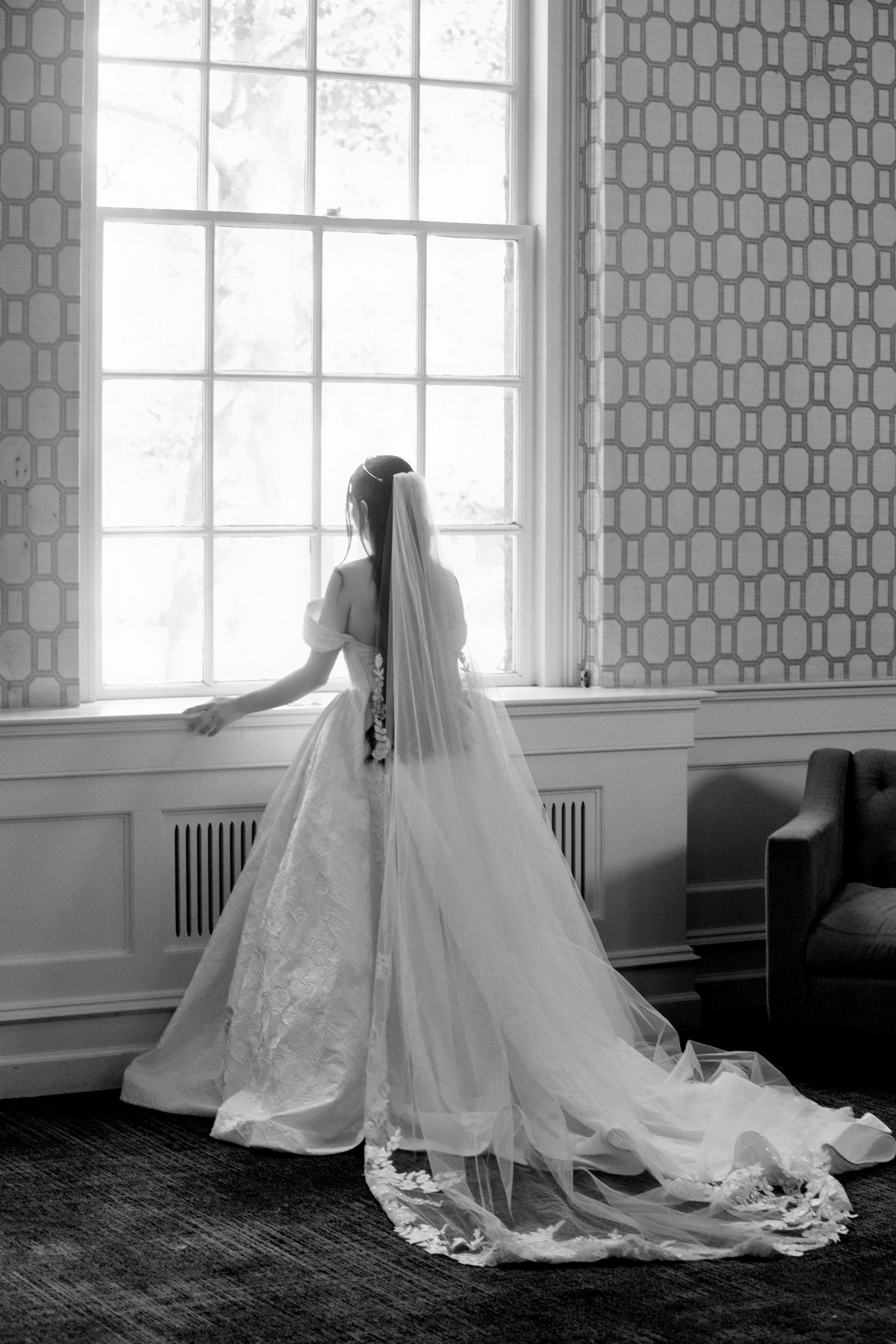 Flowing wedding dress train spreads elegantly across dark hardwood floor in black and white photo.