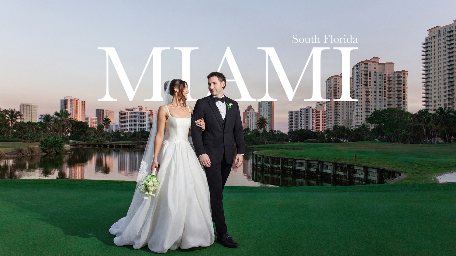 A couple in wedding attire poses on a golf course with the Miami skyline and lake in the background at sunset.