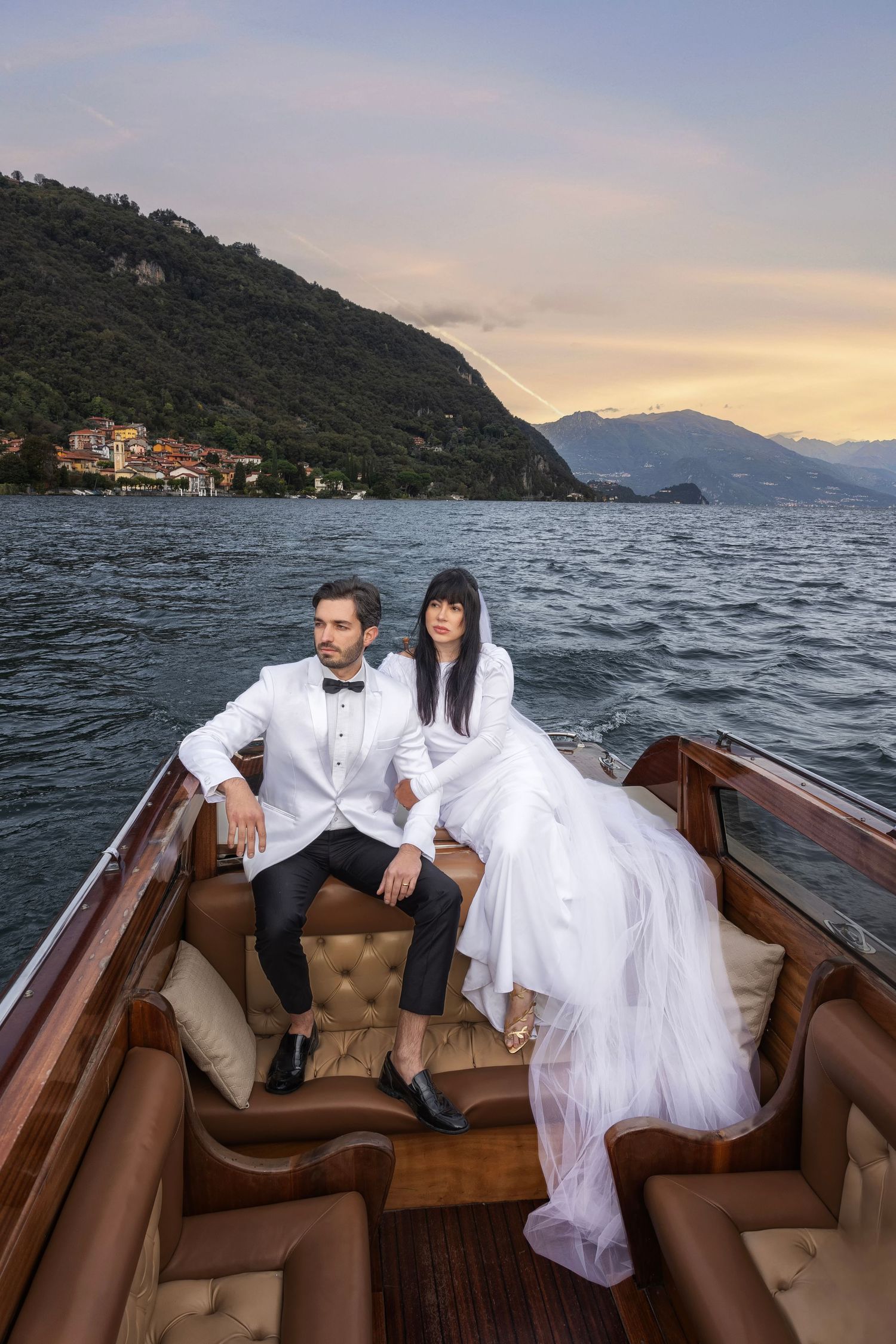 Couple enjoying a romantic boat ride on Lake Como at sunset with mountains and villas in the background.