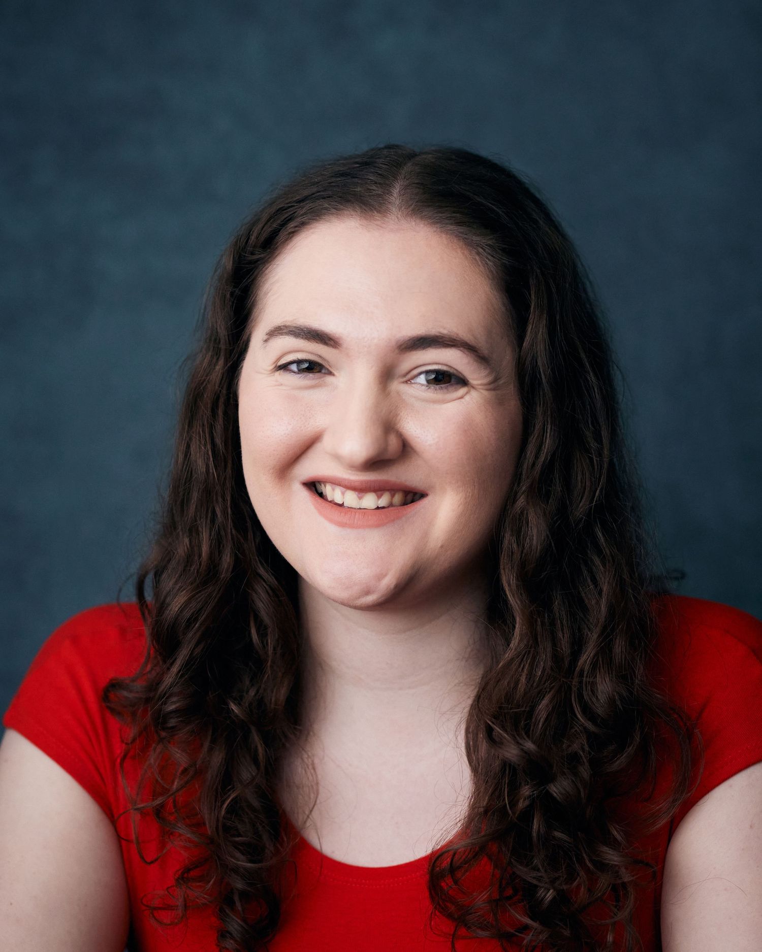 Cheerful studio headshot; woman with a bright, genuine smile against a blue backdrop.