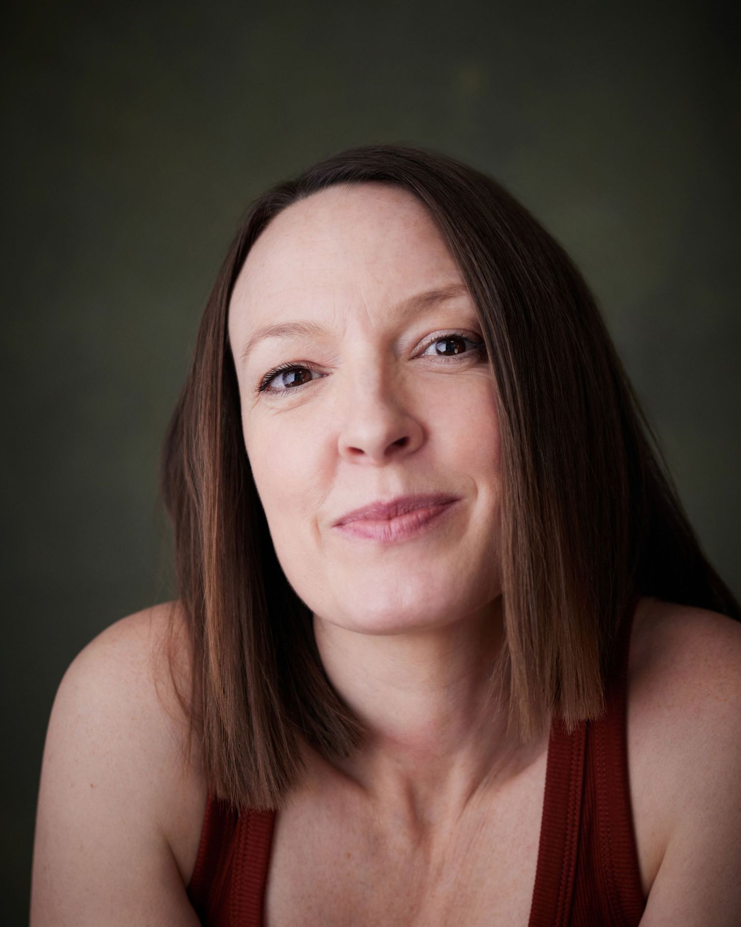 Engaging studio portrait; actress leaning forward with a curious, friendly look on a green background.