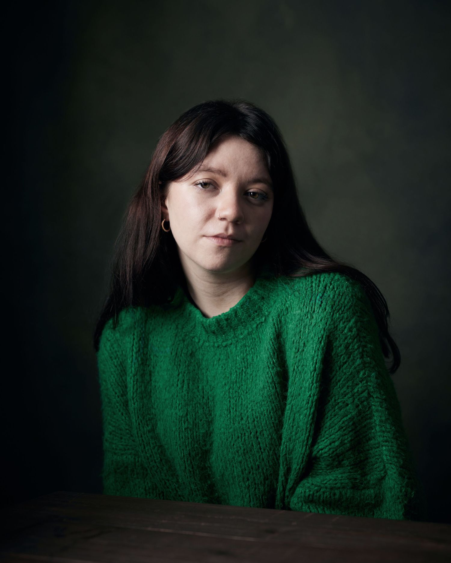 Moody headshot; woman in a green knit jumper with a defiant look.