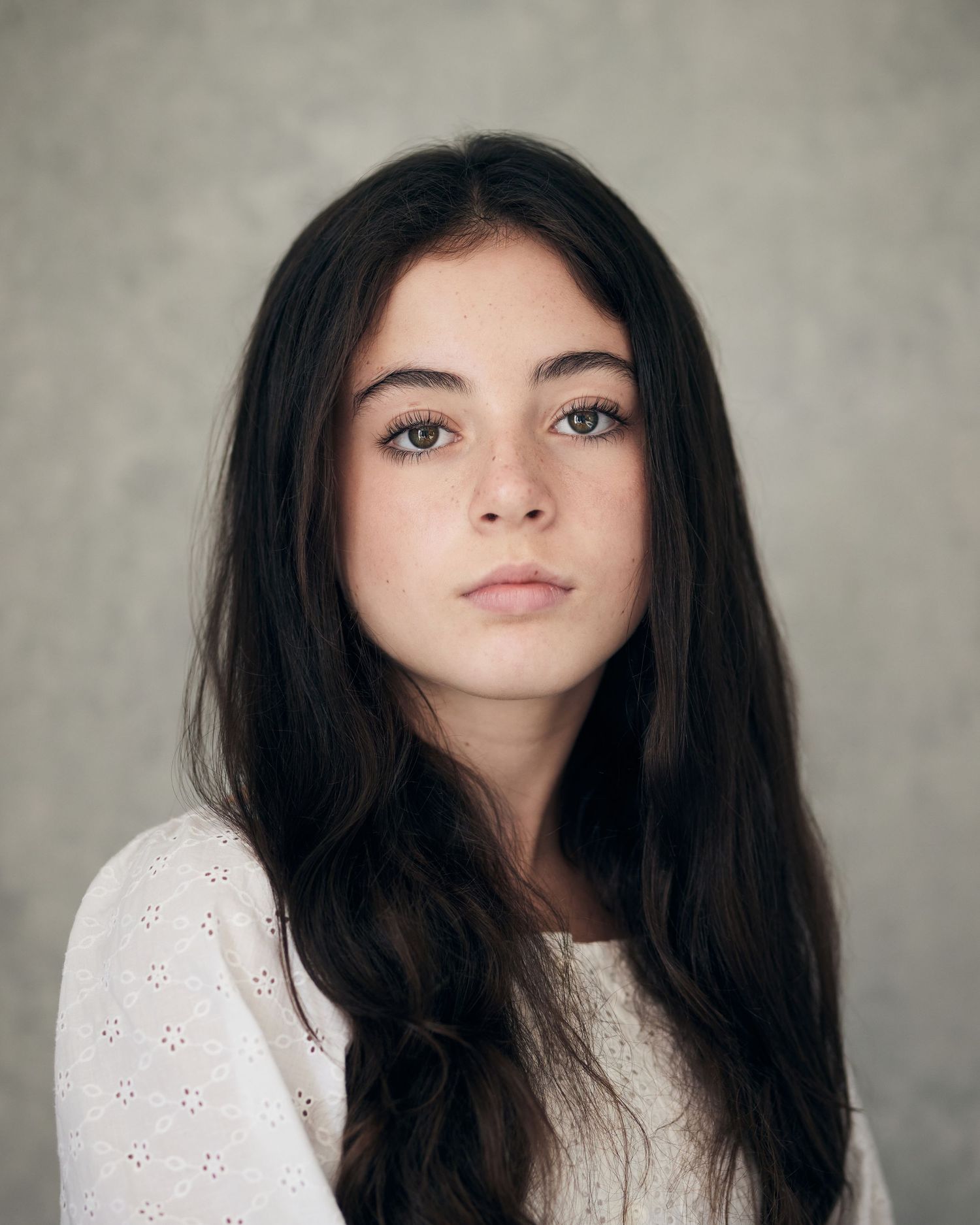 Elegant headshot; actress with a calm, centered presence on a light grey backdrop.