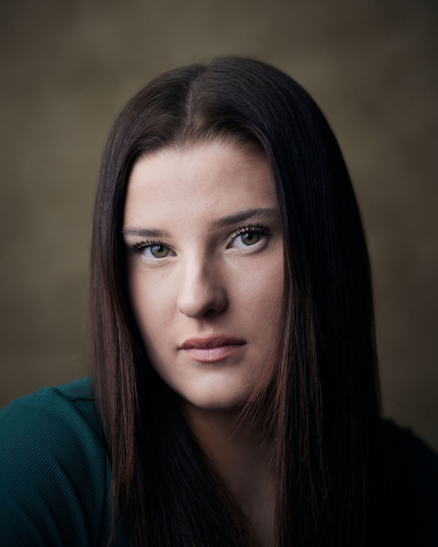 Dramatic headshot of a female actor with a piercing, intense gaze on a textured brown background.