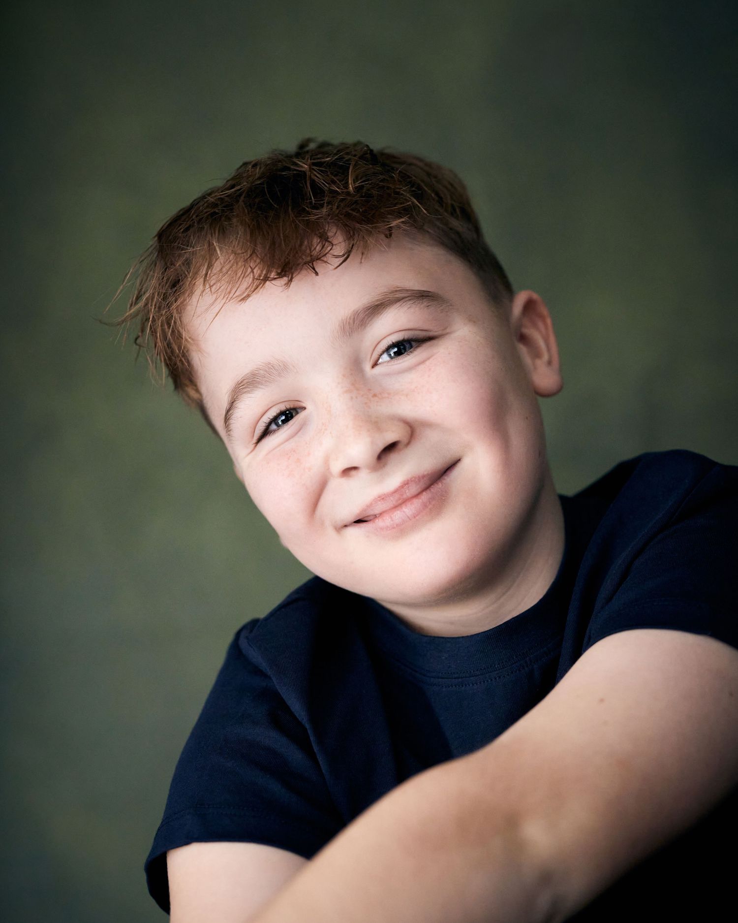 Warm studio headshot; young actor with a big, joyful smile against green.
