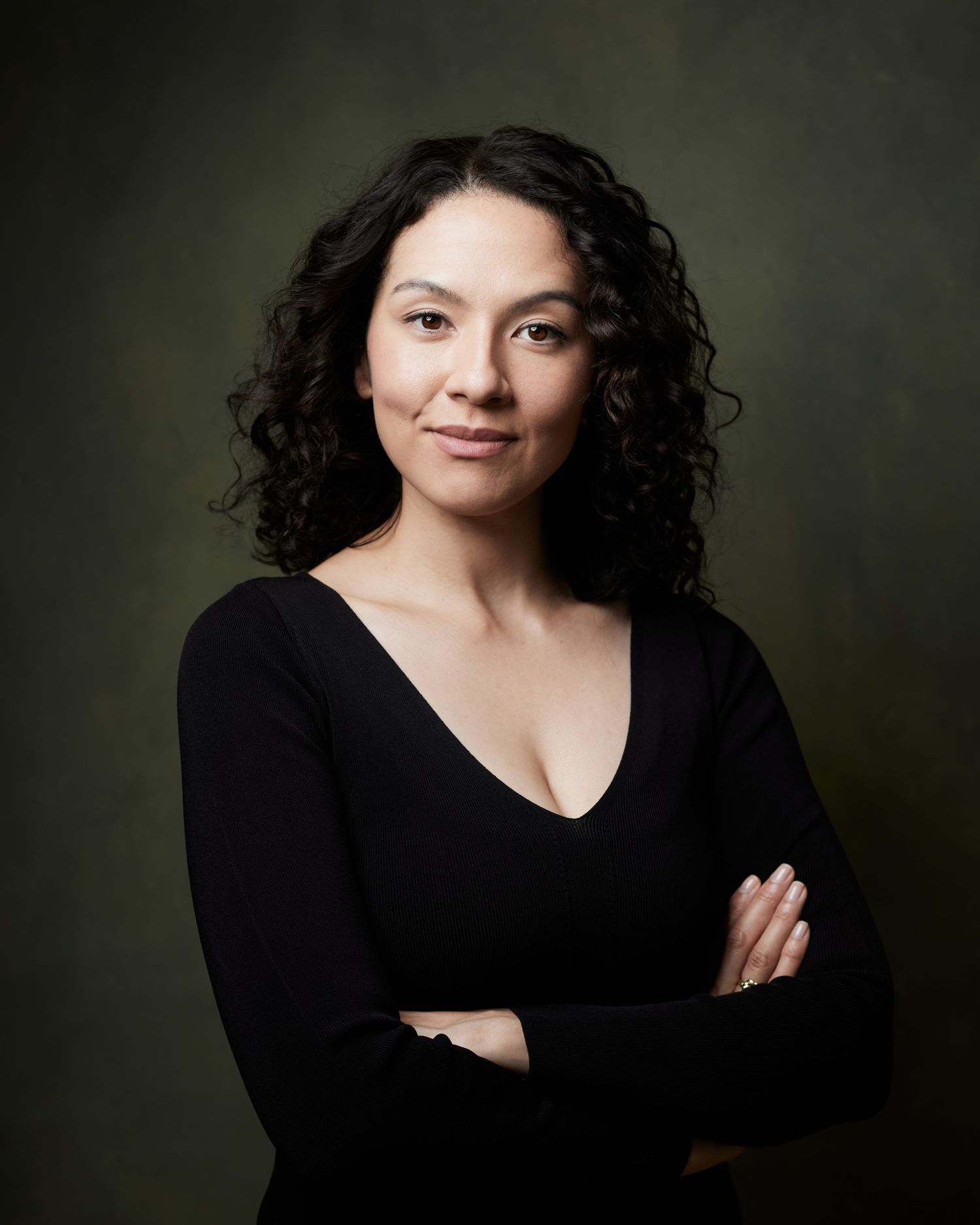 Corporate-style headshot; woman with her arms folded witha  confident expression against a green backdrop.