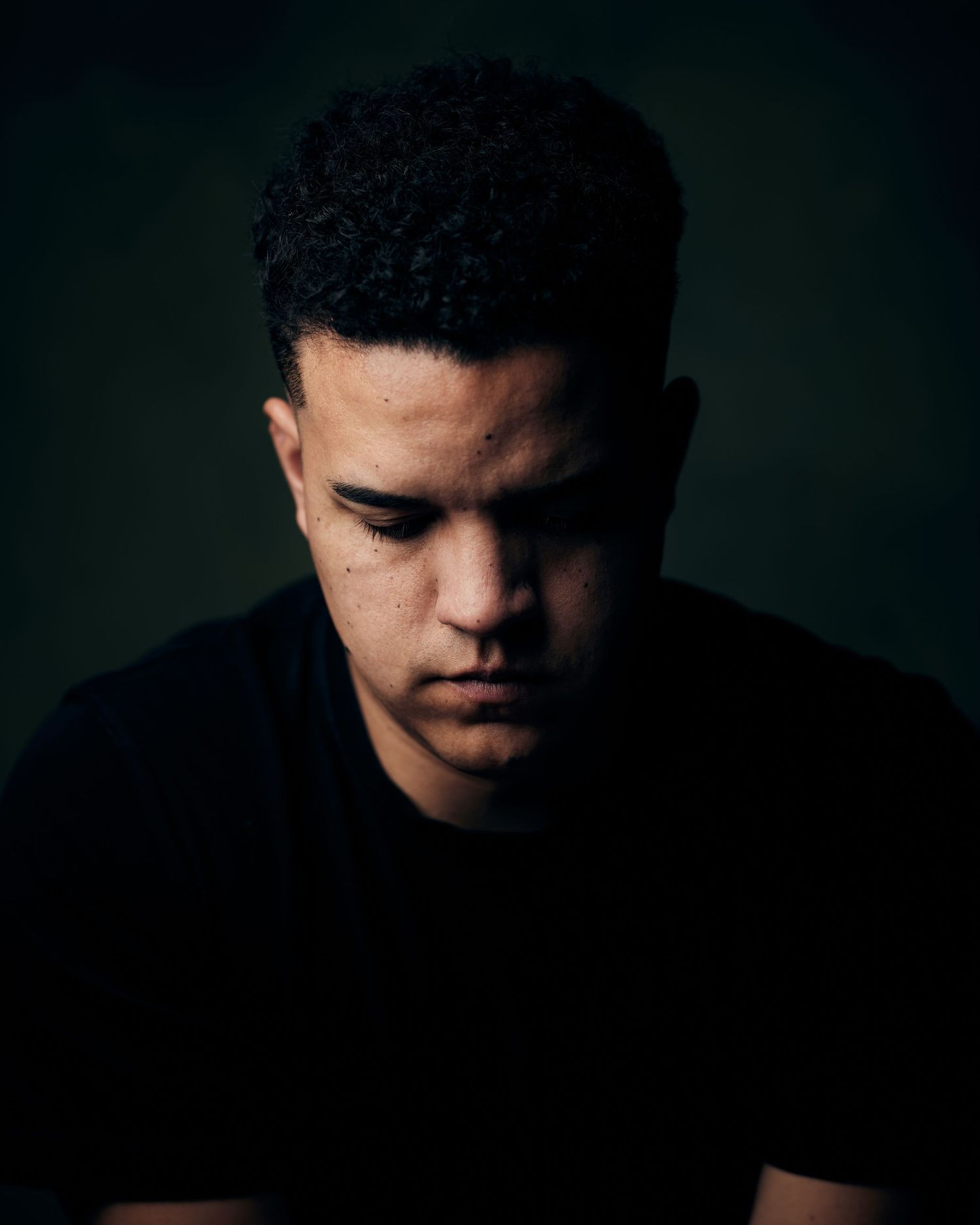 Moody actor headshot of an actor with his head down and eyes closed with deep shadows.