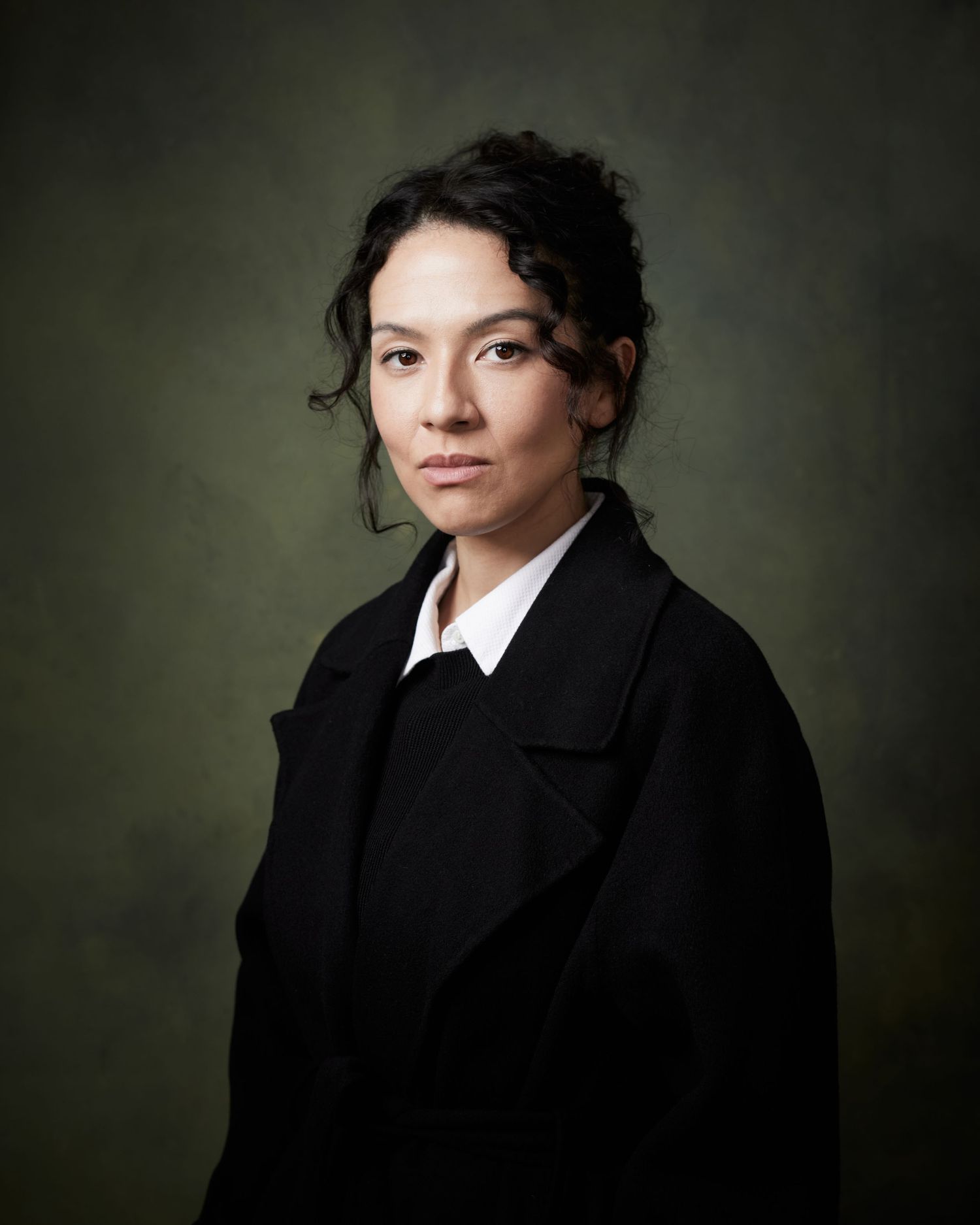 Direct-gaze portrait; actress with a sharp, ambitious look against a textured green canvas.