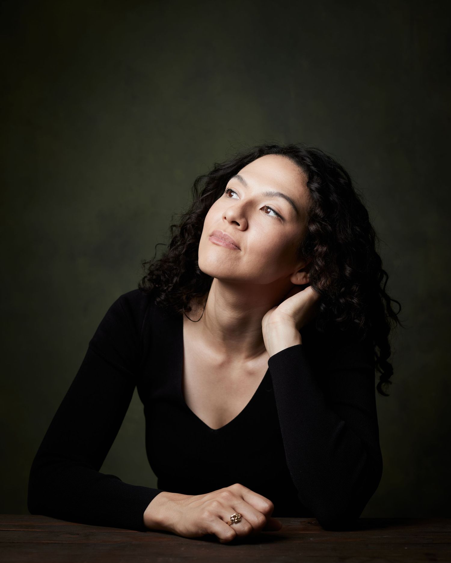 Contemplative headshot of a a female actor looking pensively off-camera against a green canvas backdrop.
