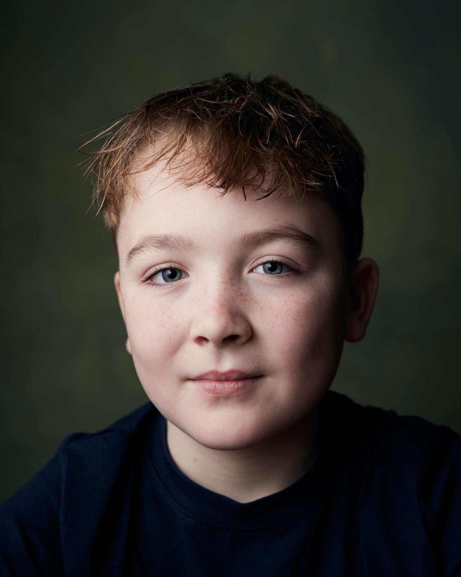 Friendly headshot; young performer with a calm, curious expression on a green canvas.