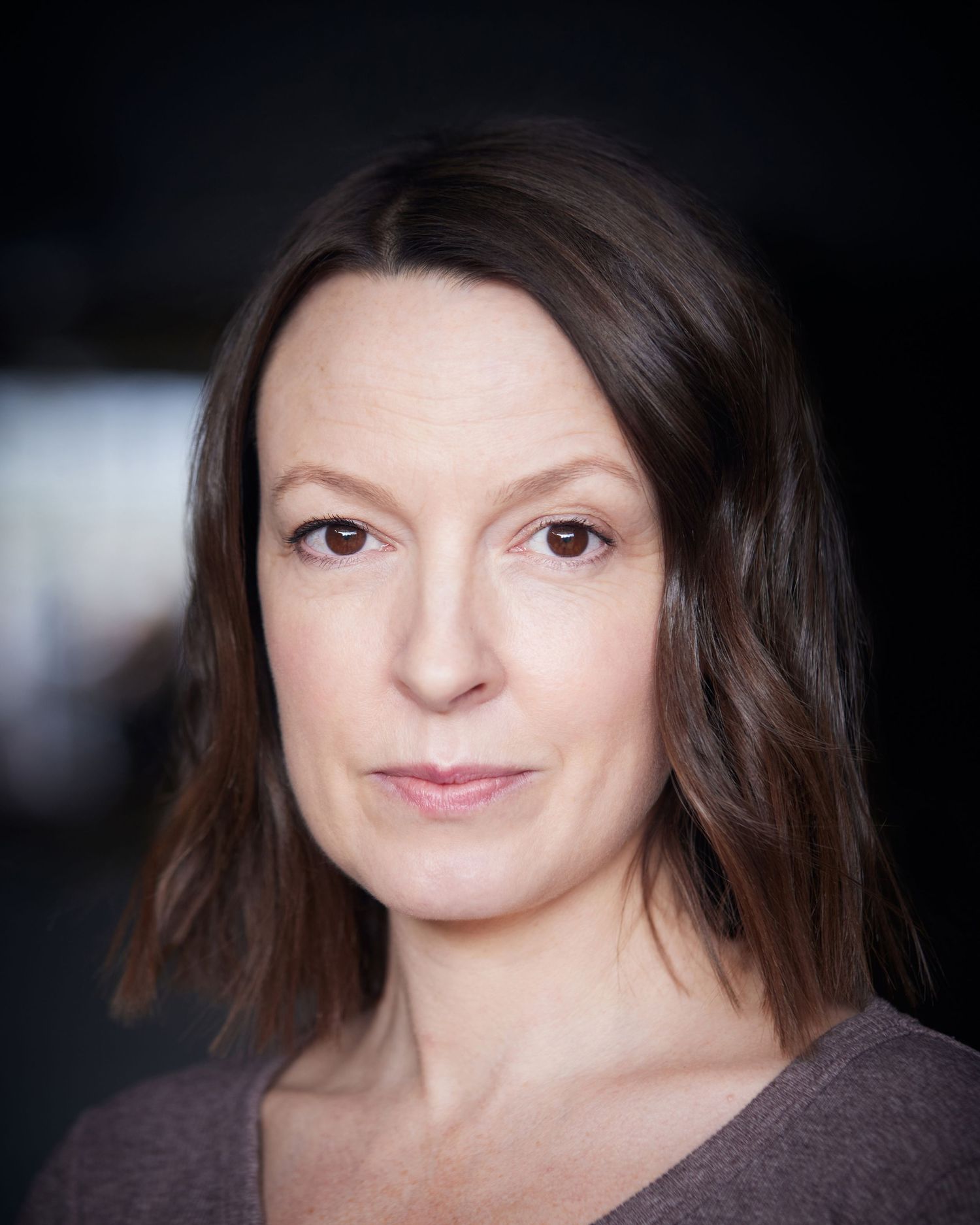 Modern professional headshot; actress with a strong, direct gaze.