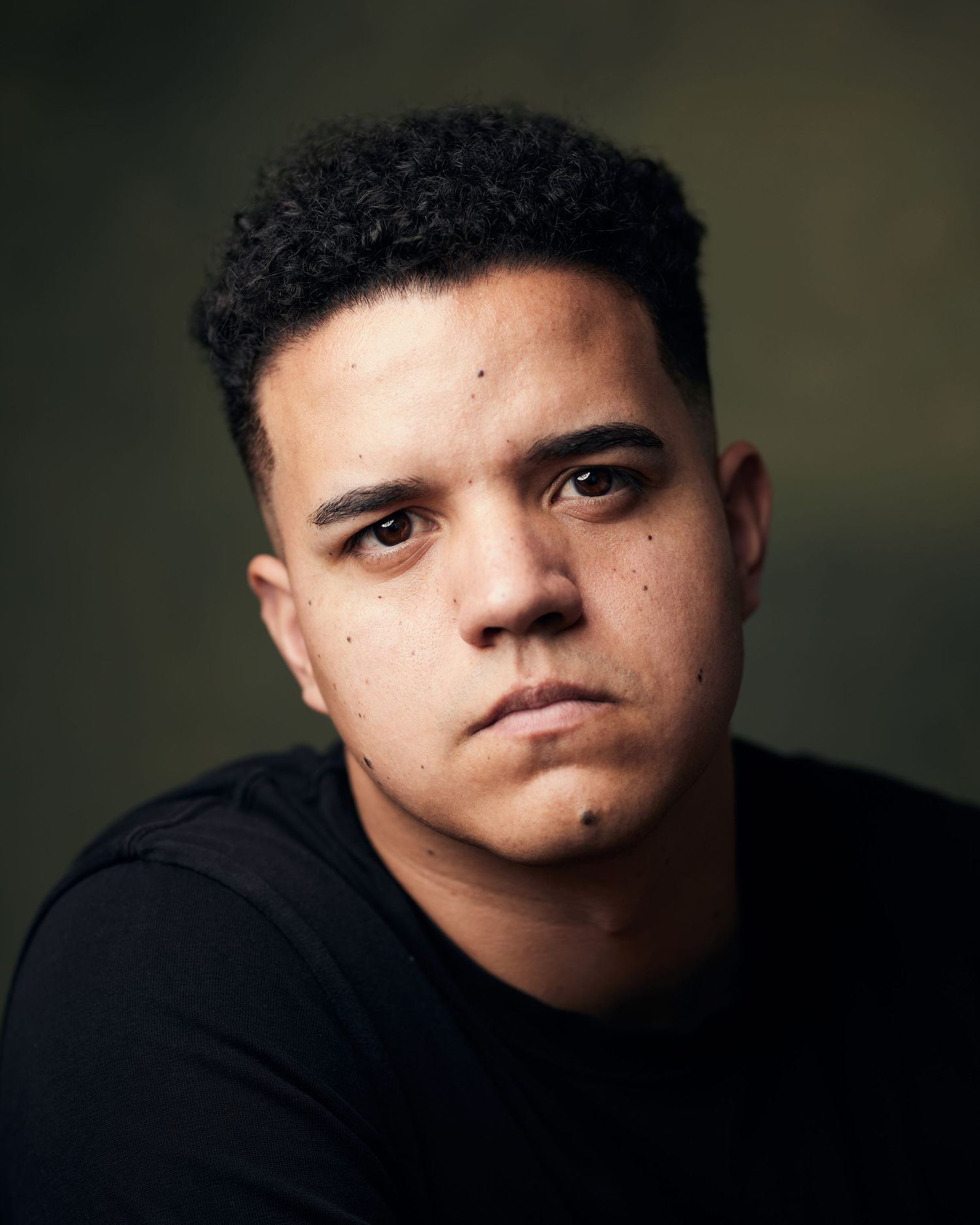 Intense dramatic close-up; male actor with a moody, somber gaze against a green background.