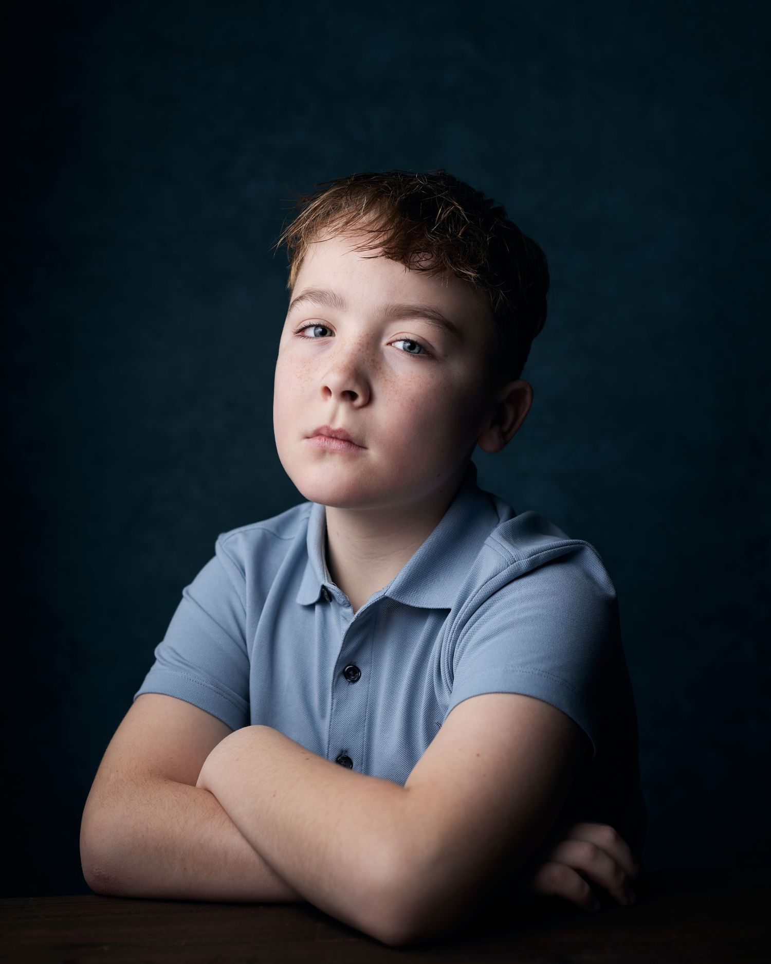 Low key headshot of a young actor with a blue canvas backdrop and strong, serious expression.
